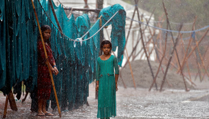 Девочки стоят под проливным дождем возле открытых прачечных в Нью-Дели