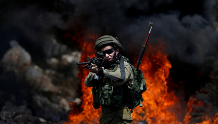 израильский солдат держит оружие в сторону палестинских демонстрантов