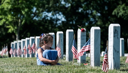 Девушка сидит перед надгробием во время Дня поминовения, когда посетители чествуют ветеранов и погибших в войне. США, штат Вирдж