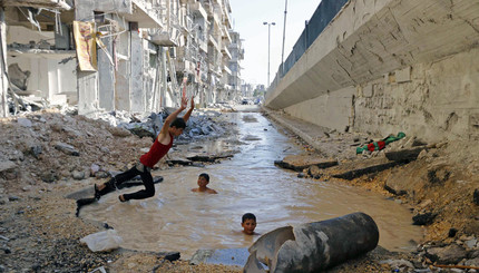 Ребята купаются в воронке от взорвавшейся бомбы в районе Аль – Шаар города Алеппо, Сирия.
