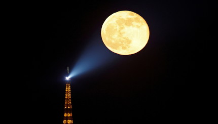 Полная луна восходит за Эйфелевой башней в Париже.