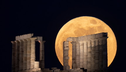 Полная луна восходит над храмом Посейдона на мысе Сунион, недалеко от Афин, Греция.