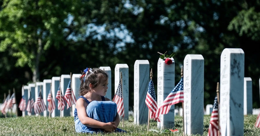 Девушка сидит перед надгробием во время Дня поминовения, когда посетители чествуют ветеранов и погибших в войне. США, штат Вирдж