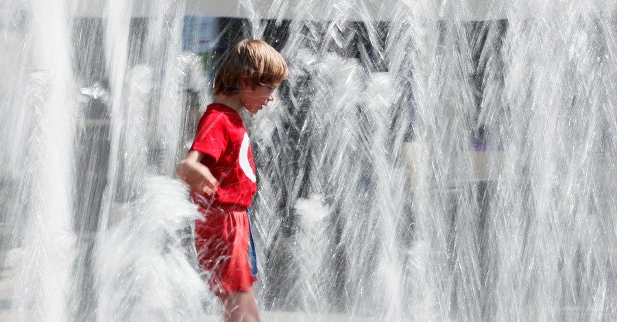 Ребёнок играет в фонтане в жаркий летний день в центре Киева, Украина
