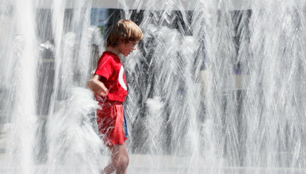Ребёнок играет в фонтане в жаркий летний день в центре Киева, Украина