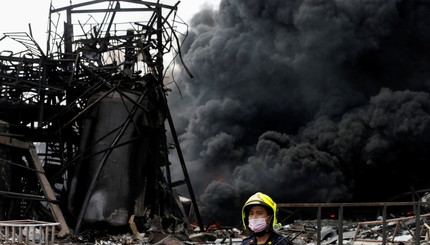 Сотрудники службы экстренной помощи наблюдают, как дым поднимается над пластиковой фабрикой после взрыва в Самутпракане, недалек