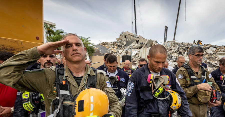 Член израильской поисково-спасательной группы (слева) отдает честь перед обломками, которые когда-то были южными башнями Шамплей