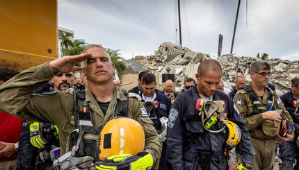 Член израильской поисково-спасательной группы (слева) отдает честь перед обломками, которые когда-то были южными башнями Шамплей